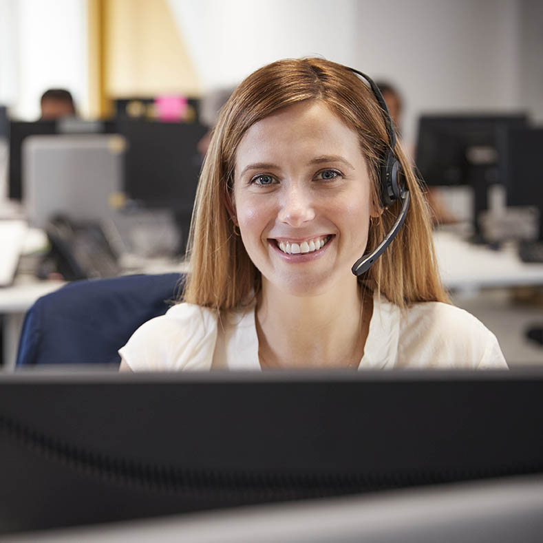 Young woman working at computer with headset in busy office